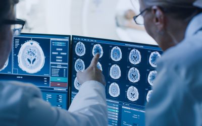 In Control Room Doctor and Radiologist Discuss Diagnosis while Watching Procedure and Monitors Showing Brain Scans Results, In the Background Patient Undergoes MRI or CT Scan Procedure. In Control Room Doctor and Radiologist Discuss Diagnosis while Watching Procedure and Monitors Showing Brain Scans Results, In the Background Patient Undergoes MRI or CT Scan Procedure.